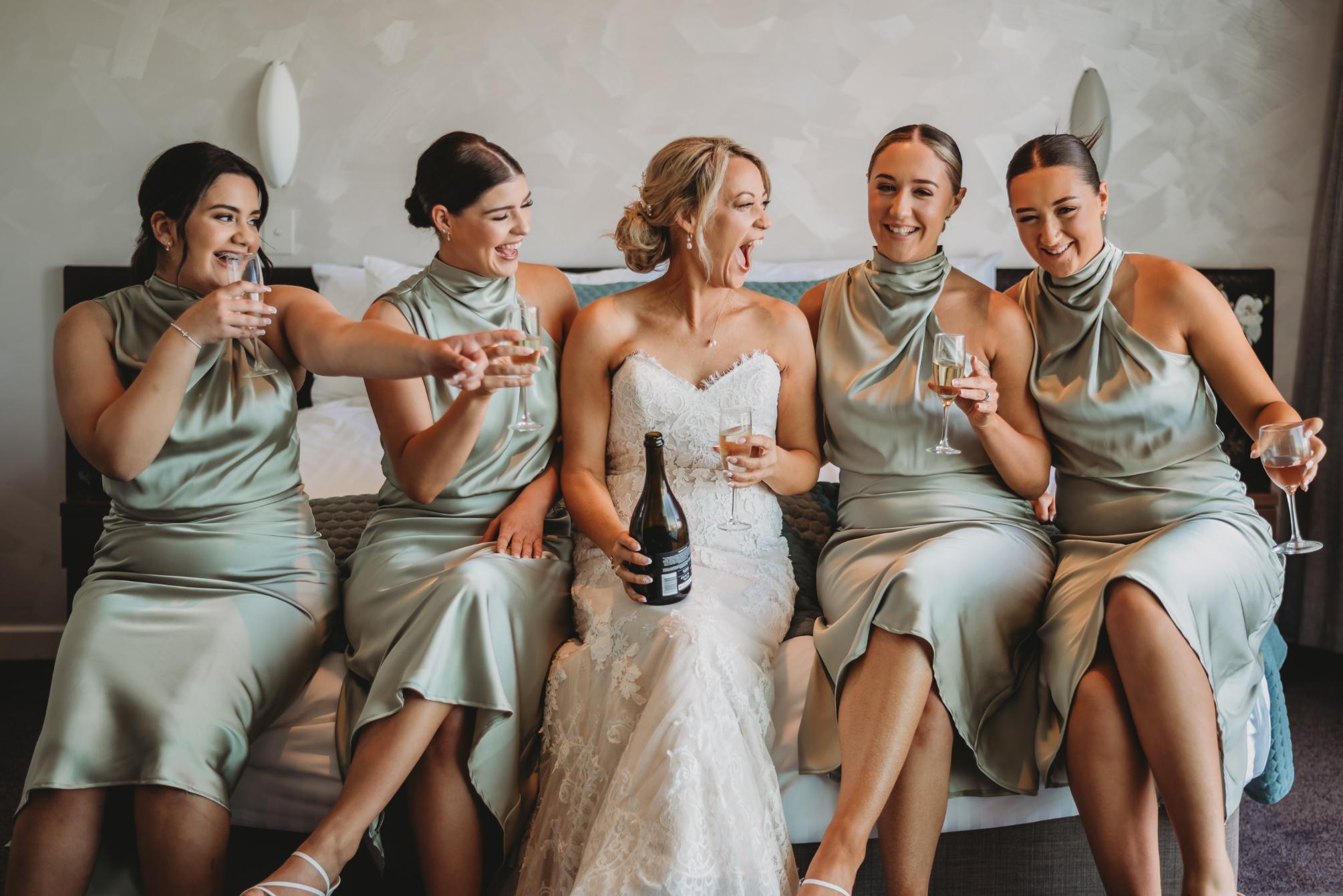 Bridal party toasting champagne in sage green dresses, natural spray tan visible
