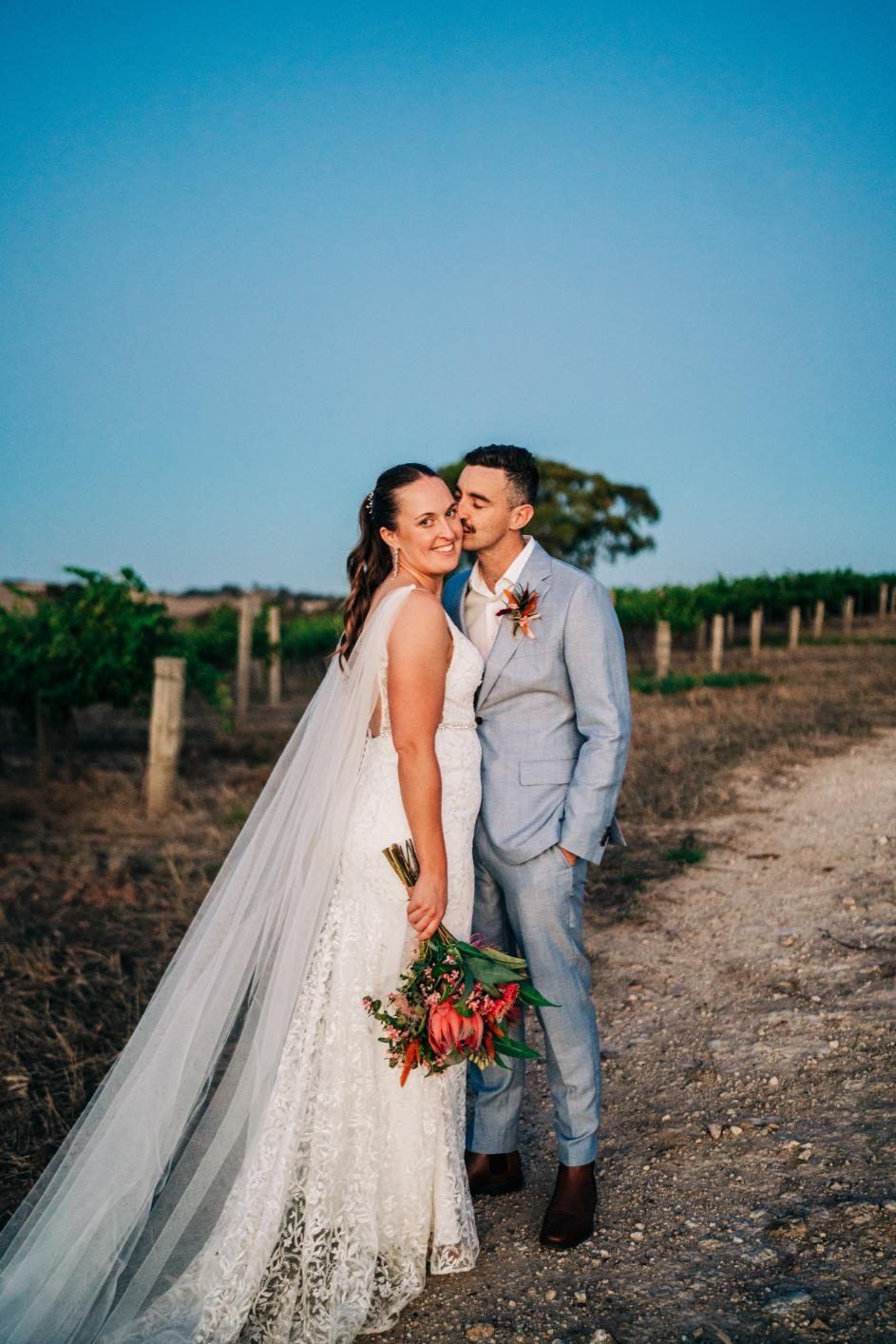 Bride and groom kissing in a vineyard under open sky